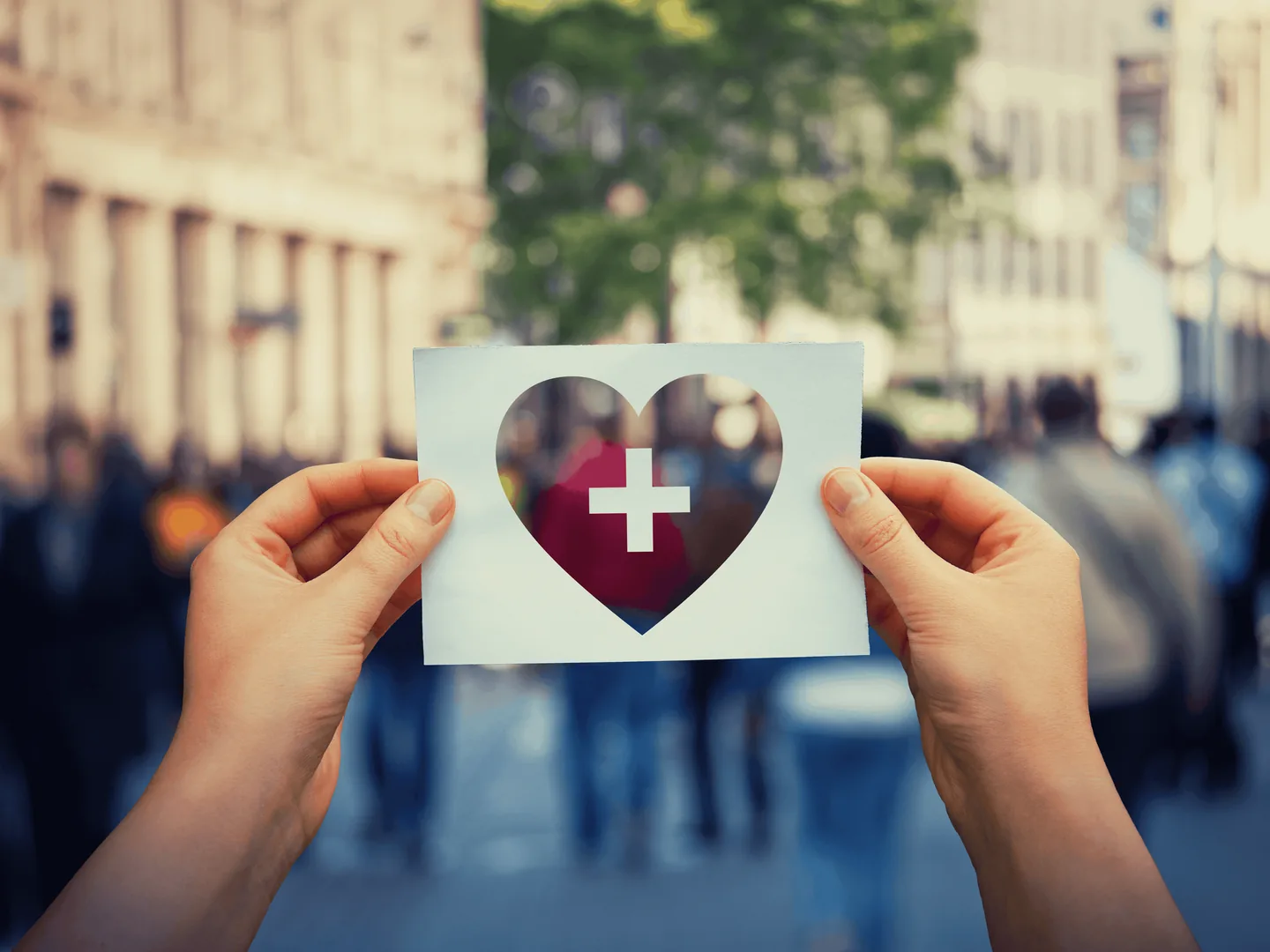 A person holding a card with a heart and a medical cross cut out of it